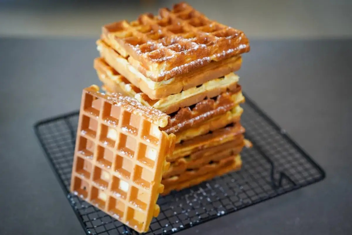 Pile de gaufres dorées saupoudrées de sucre glace, prêtes à être dégustées. Une recette gaufre parfaite pour le petit-déjeuner ou le goûter.