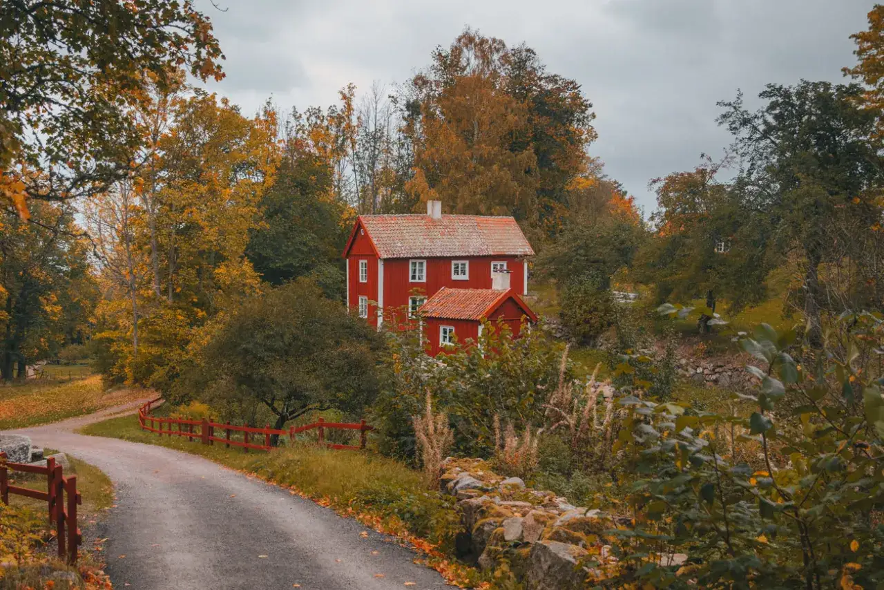 Rotes Haus in Schweden im September. Herbstlaub und grauer Himmel deuten auf typisches schwedisches Herbstwetter hin.