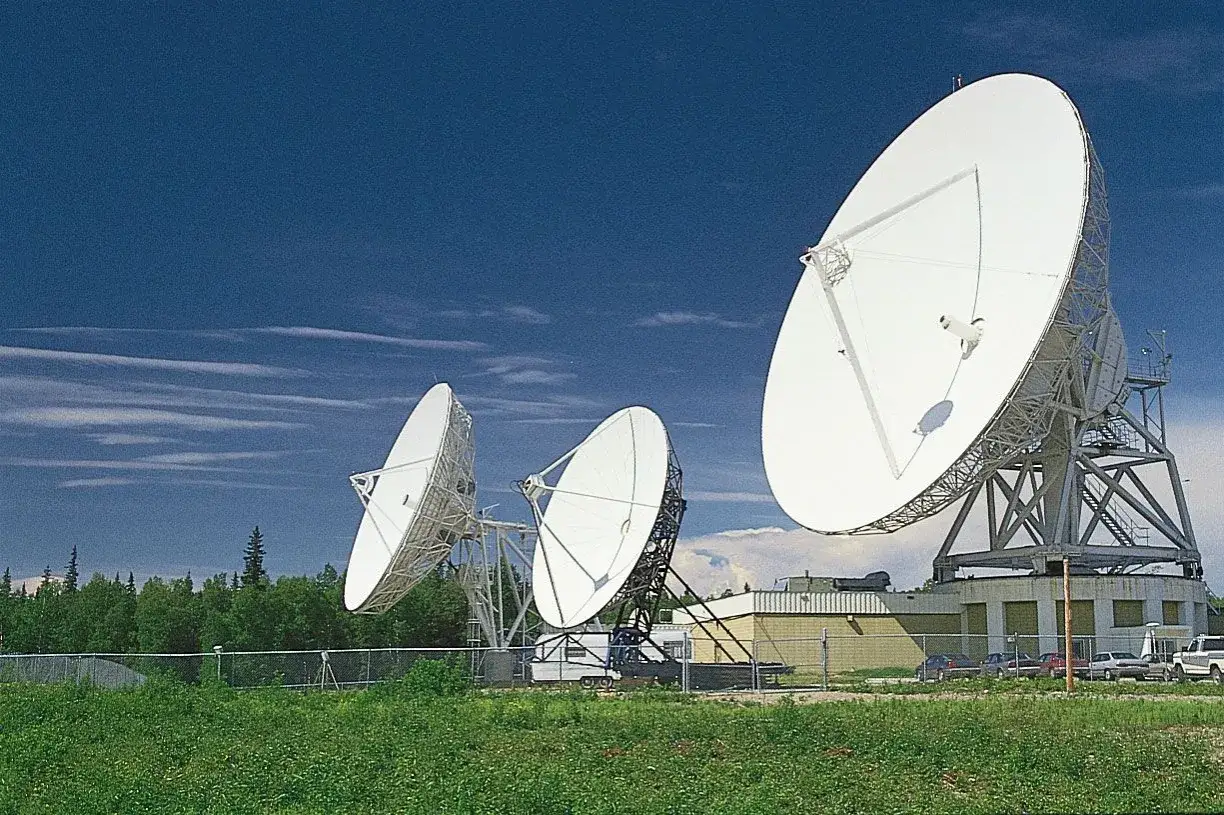 Trzy ogromne anteny satelitarne, świadczące o fascynującym zastosowaniu fal radiowych w komunikacji i badaniach kosmosu, na tle błękitnego nieba.