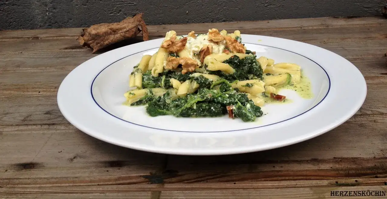 Herzhafte Spinat Ricotta Tortellini mit Walnüssen und cremiger Sauce auf einem weißen Teller.