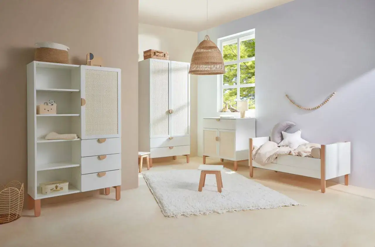 Przytulny pokój dziecka w stylu boho. Białe meble z rattanowymi wstawkami, łóżeczko, regał i szafa tworzą harmonijną całość.
