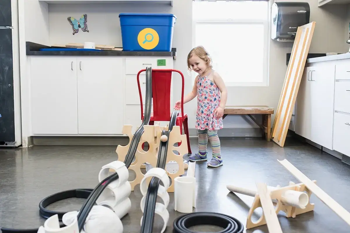 Niña interactúa con un proyecto STEAM primaria, construyendo una rampa con tubos y madera.