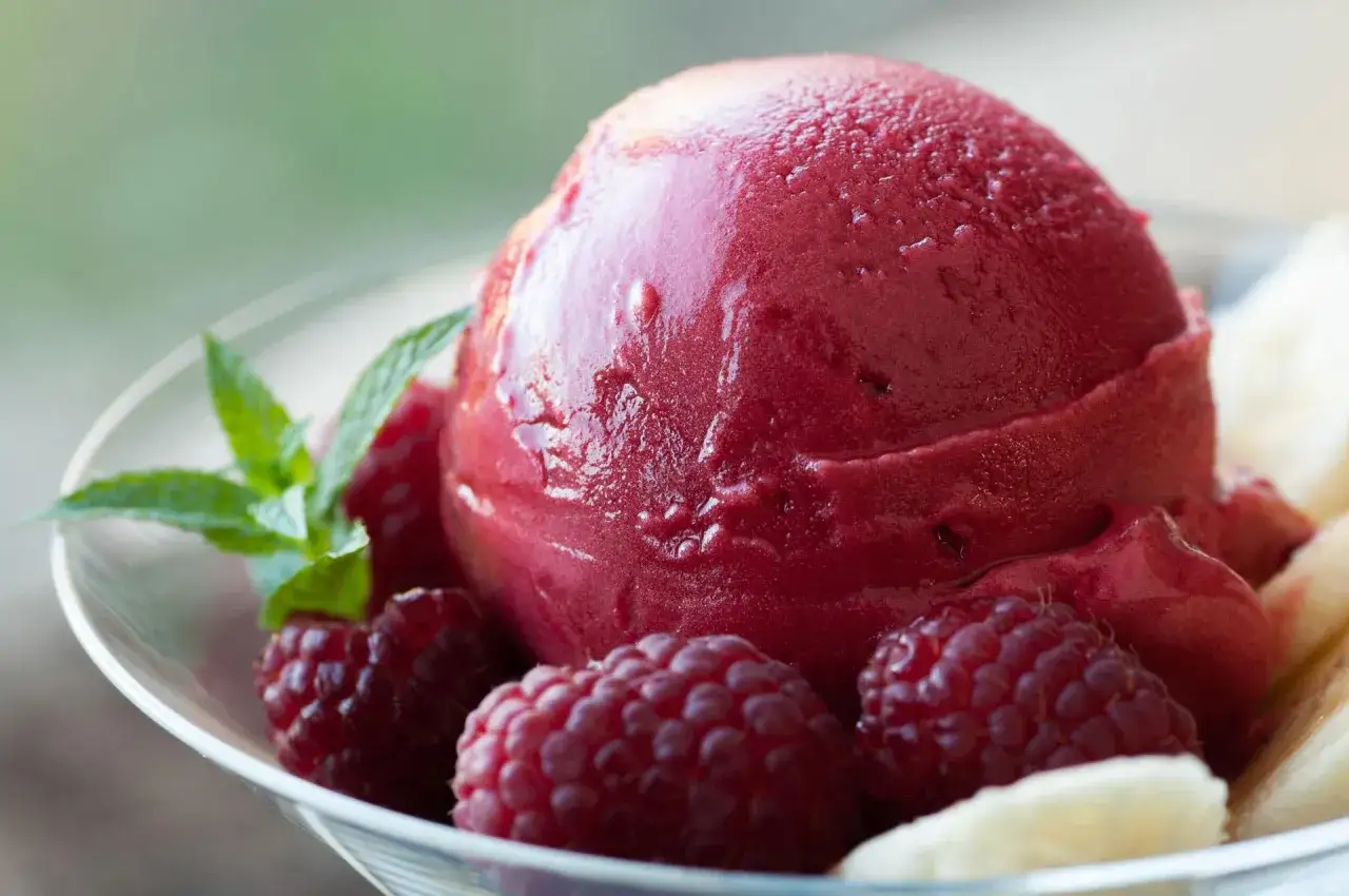 Jak zrobić sorbet malinowy? Pyszny, mrożony deser z malinami, bananem i miętą w szklanej miseczce.