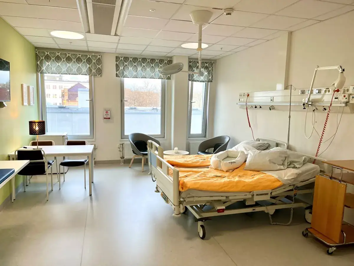 Ett modernt sjukhusrum med tv&aring; s&auml;ngar, en matplats och f&ouml;nster. H&auml;r kan man fundera p&aring; vad betyder bb, kanske en nyf&ouml;dd bebis v&auml;ntar.