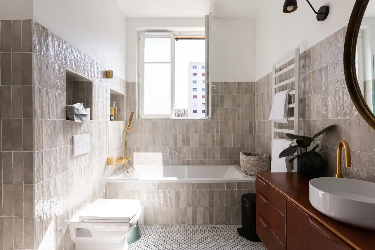 Salle de bain moderne avec carrelage zellige gris, baignoire, lavabo sur meuble en bois et robinetterie dor&eacute;e. Inspiration zellige salle de bain.