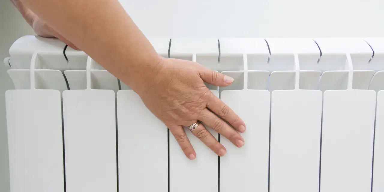 Main posée sur un radiateur blanc, vérifiant la température pour éviter le hors gel et optimiser la consommation.