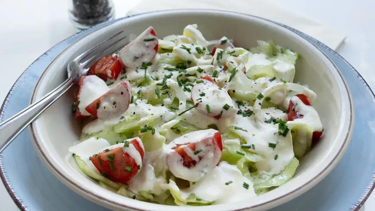 Frischer Tomaten-Gurken-Salat mit cremiger So&szlig;e und Schnittlauch garniert, bereit zum Genie&szlig;en.