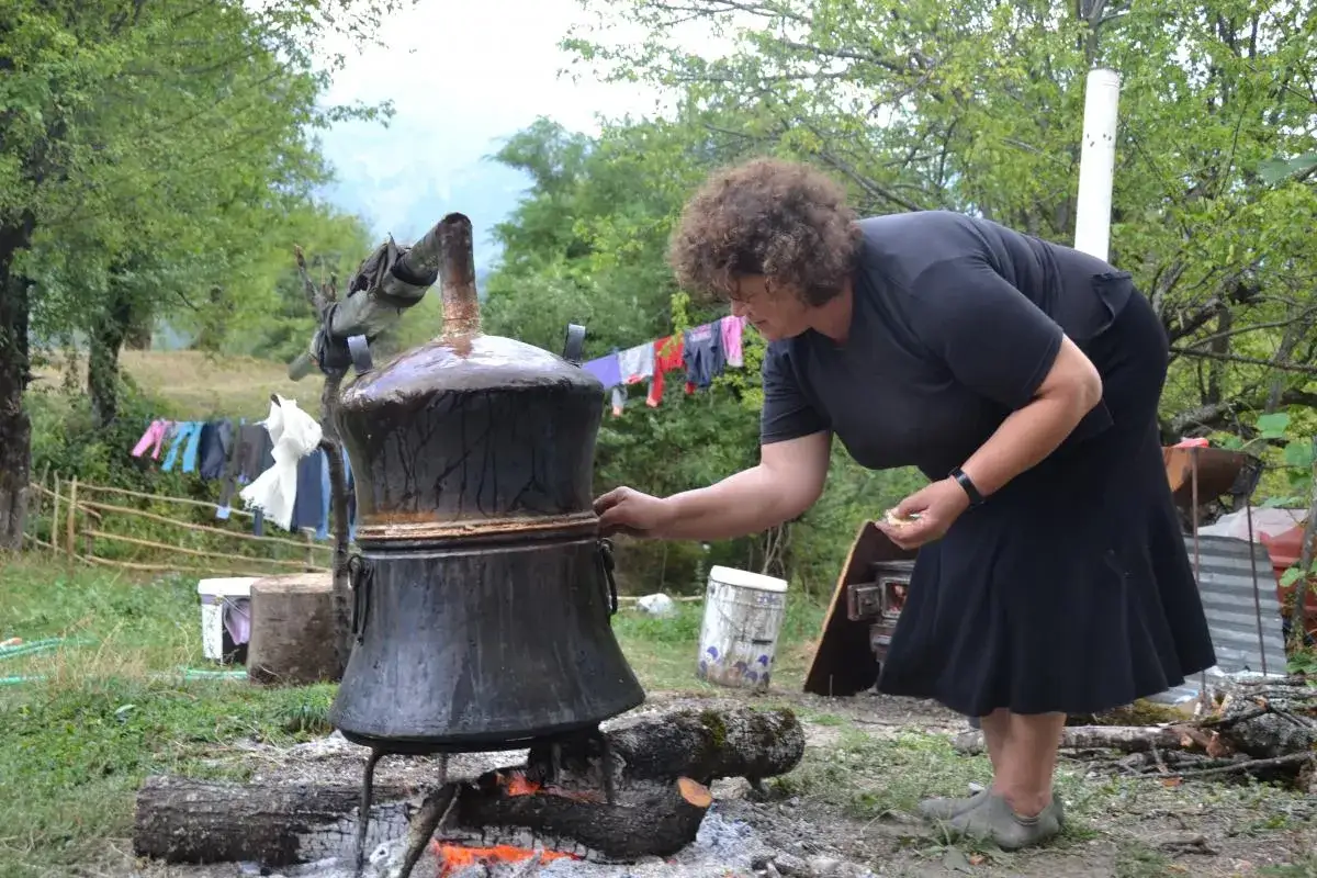 Frau überwacht die Destillation, die zeigt, woher Raki kommt. Wäsche trocknet im Hintergrund.