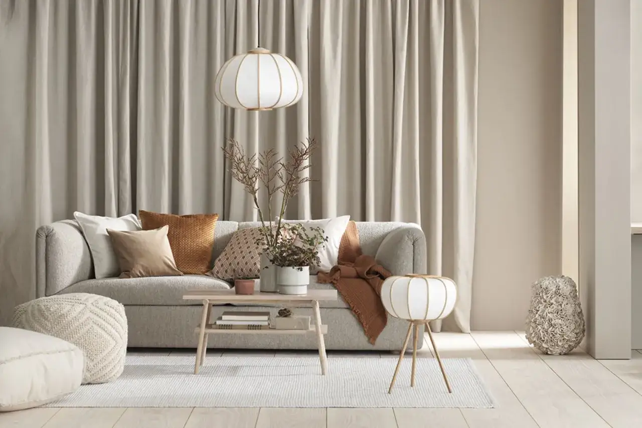 Ein gemütliches Wohnzimmer mit einem grauen Sofa, das mit Kissen in warmen Erdtönen und einem orangefarbenen Überwurf kombiniert wird.