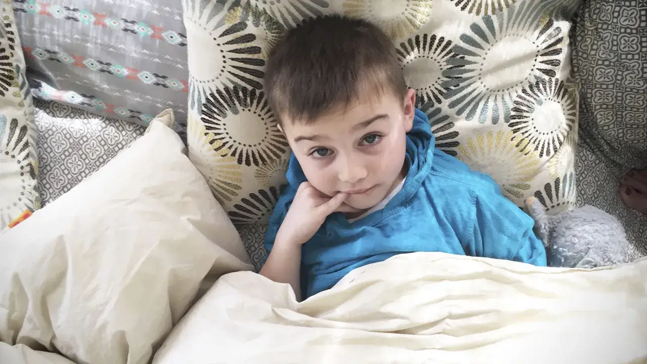 Niño con tos, acurrucado en la cama, esperando un remedio milagroso para la tos en niños.