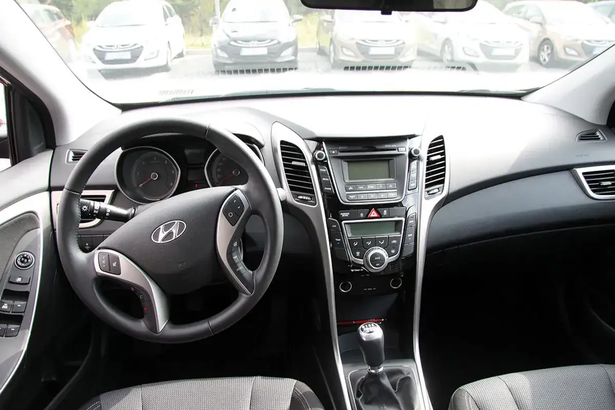 Wnętrze Hyundai i30 2015: kierownica, deska rozdzielcza z radiem i nawiewami, dźwignia zmiany biegów.