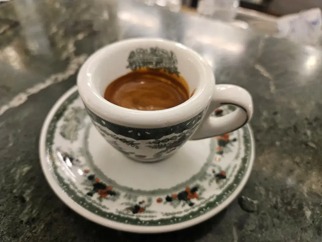 Una tazzina di ceramica bianca con decorazioni verdi e arancioni contiene un buon caffè espresso con una crema invitante.