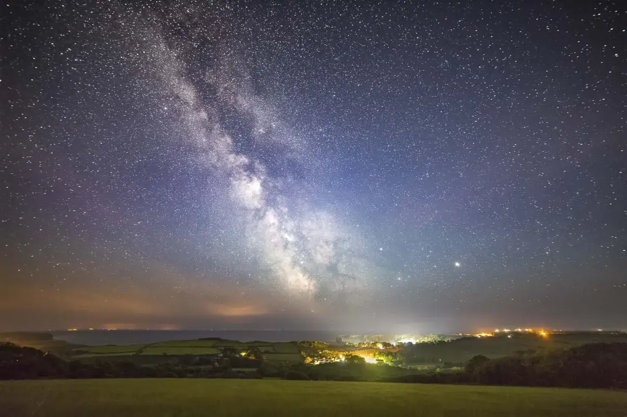 Droga Mleczna nad oświetloną wioską. Idealny widok, by zacząć przygodę z astrofotografią.