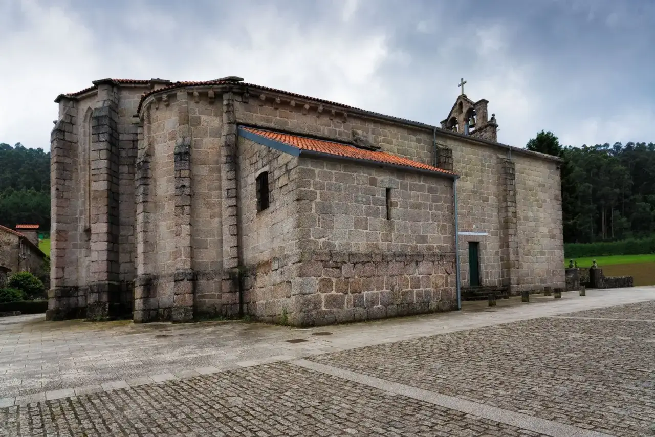 El monasterio de Soandres, con sus muros de piedra y tejados naranjas, se alza bajo un cielo nublado, rodeado de vegetación.