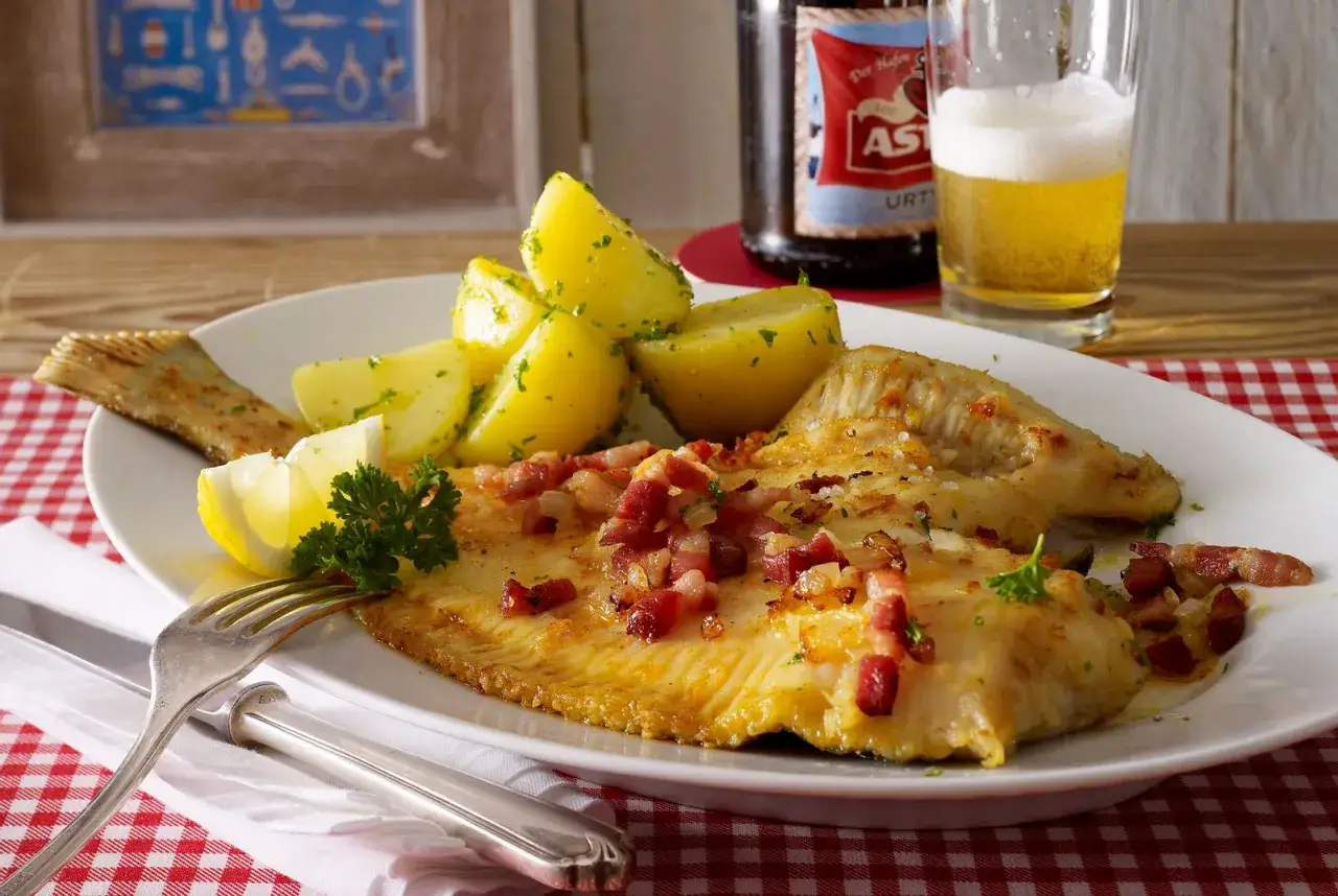 Scholle Finkenwerder Art mit Salzkartoffeln, Speck und Zwiebeln, garniert mit Petersilie und Zitrone. Dazu ein Glas Bier.