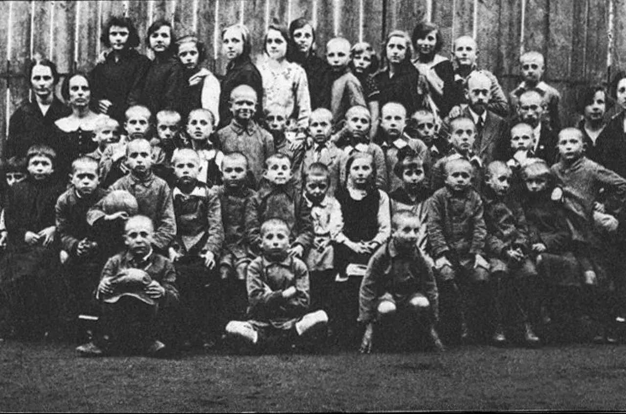Dzieci z sierocińca, jak na korczak cytaty o dziecku, patrzą w obiektyw. Wśr&oacute;d nich dorośli, być może opiekunowie.