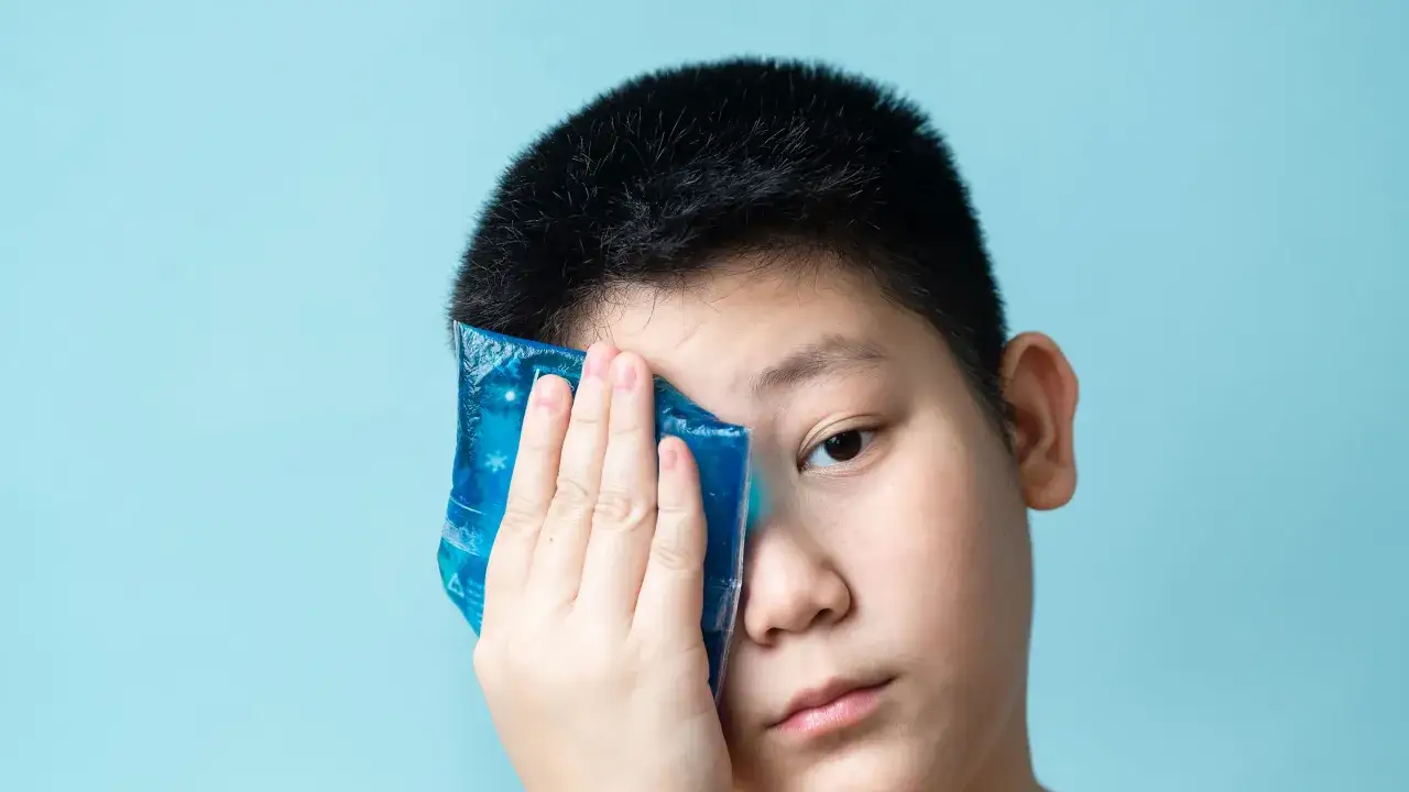 Ragazzo con impacco freddo sull'occhio, forse per congiuntivite allergica quanto dura.