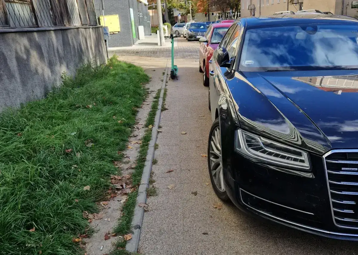 Czarny sedan zaparkowany na chodniku, obok zielona hulajnoga. Może to być podstawa do mandatu art. 97 k.w. w zw. z art. 47 p.r.d.