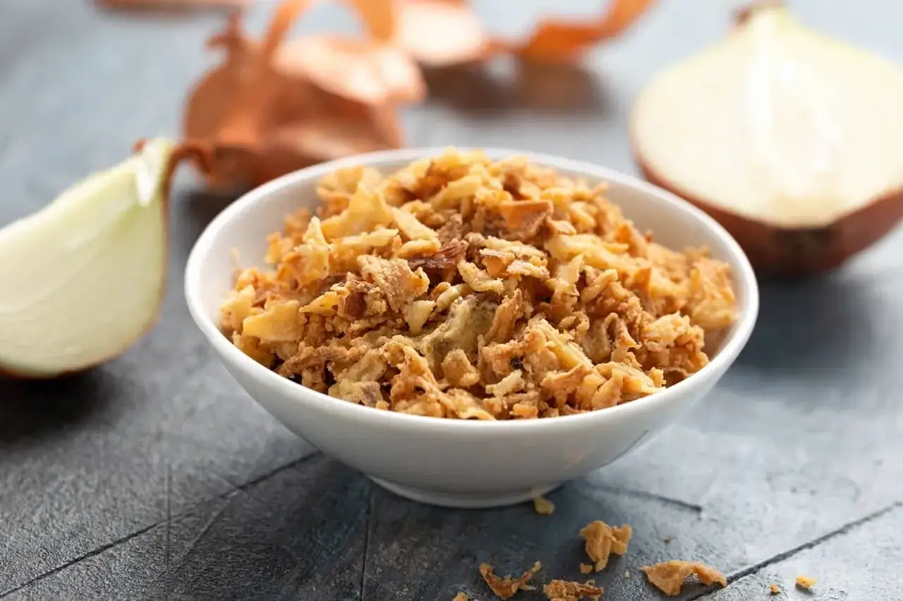 Un bol de oignon crispy doré et croustillant, entouré d'oignons frais coupés.