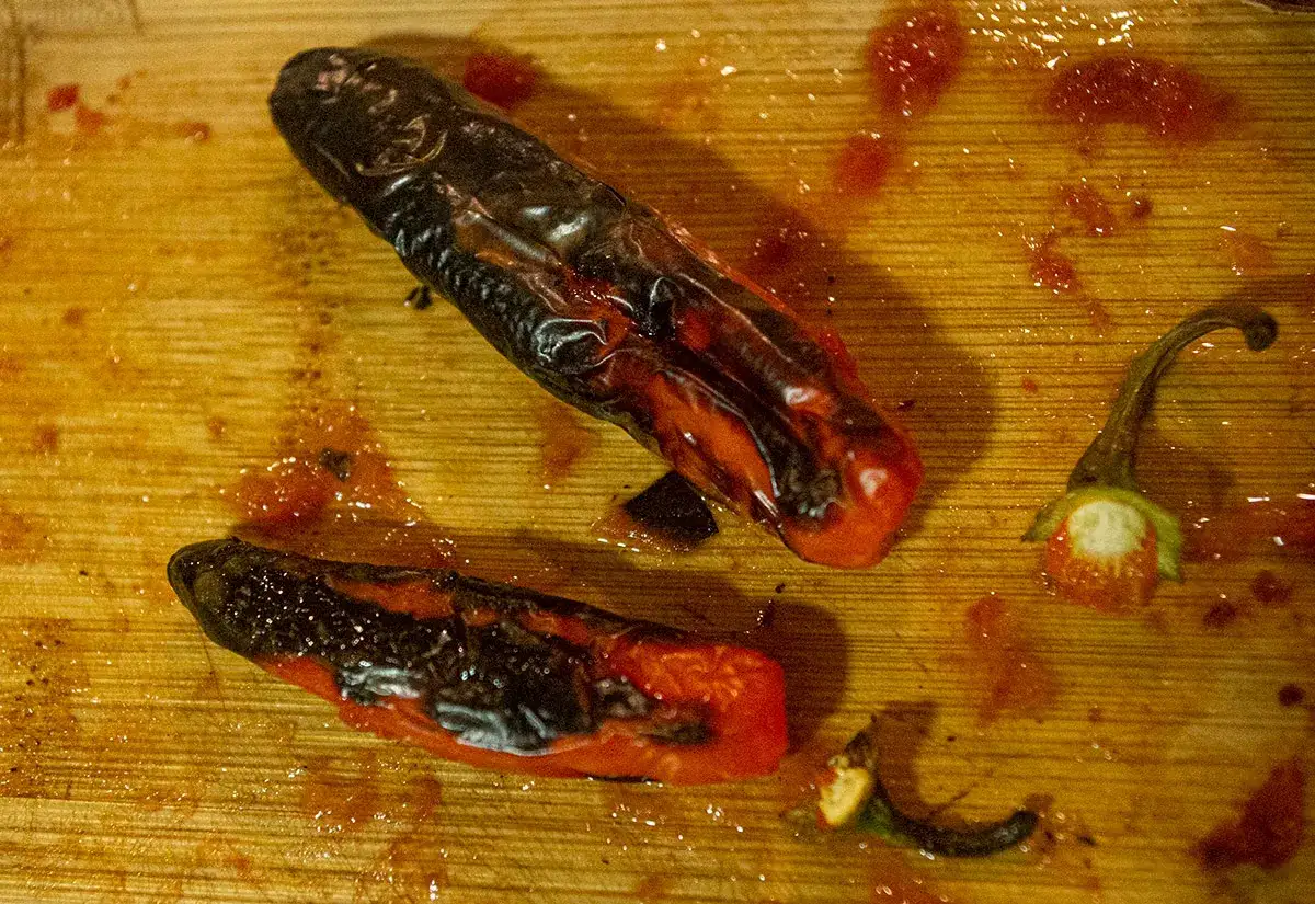 Tv&aring; rostade chilis, en hel och en delad, ligger p&aring; en tr&auml;sk&auml;rbr&auml;da med chilis&aring;s.