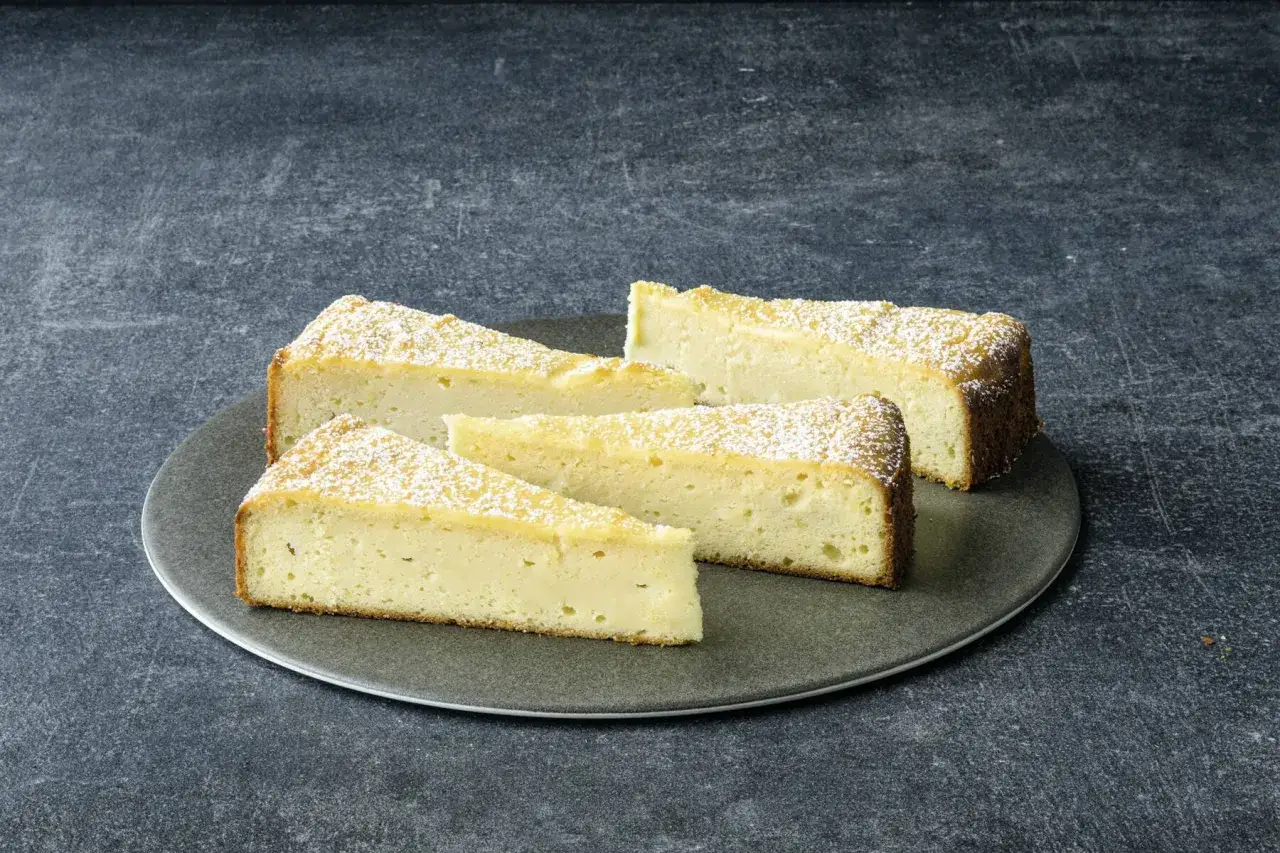 Saftige Scheiben eines Ricotta Mandel Kuchens, best&auml;ubt mit Puderzucker, auf einem grauen Teller.