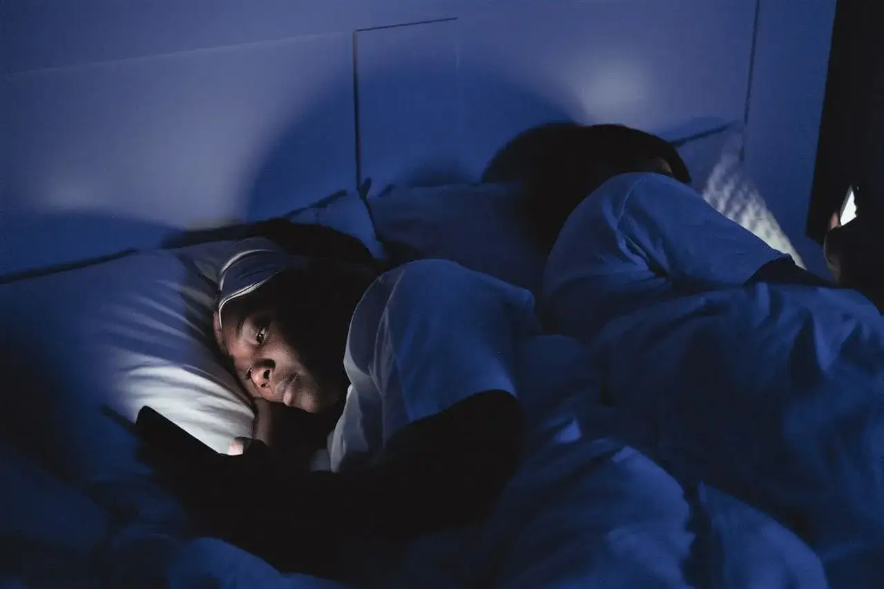 Eine Frau liegt im Bett, ihr Handy leuchtet im Dunkeln. Sie fragt sich: warum wache ich immer um 3 Uhr auf?