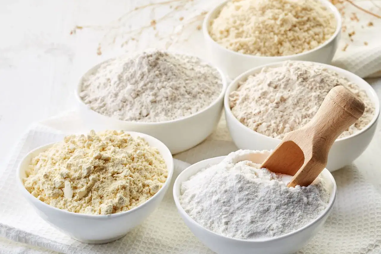 Cinq bols de diff&eacute;rentes farines, dont une farine de bl&eacute; CRC, sont pr&eacute;sent&eacute;s sur un tissu blanc. Une petite pelle en bois est dans le bol de farine blanche.