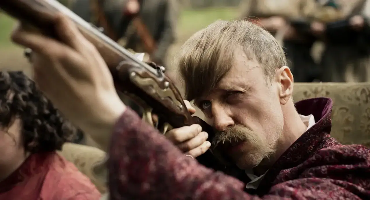 Łukasz Simlat w filmach, celuje z karabinu, gotowy do akcji.