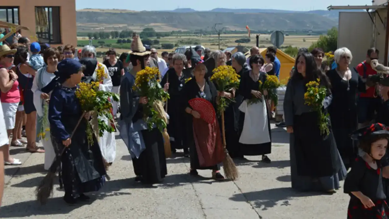 Gente disfrazada de brujas, con escobas y ramos de flores amarillas, desfila en la fiesta de las brujas de Trasmoz.