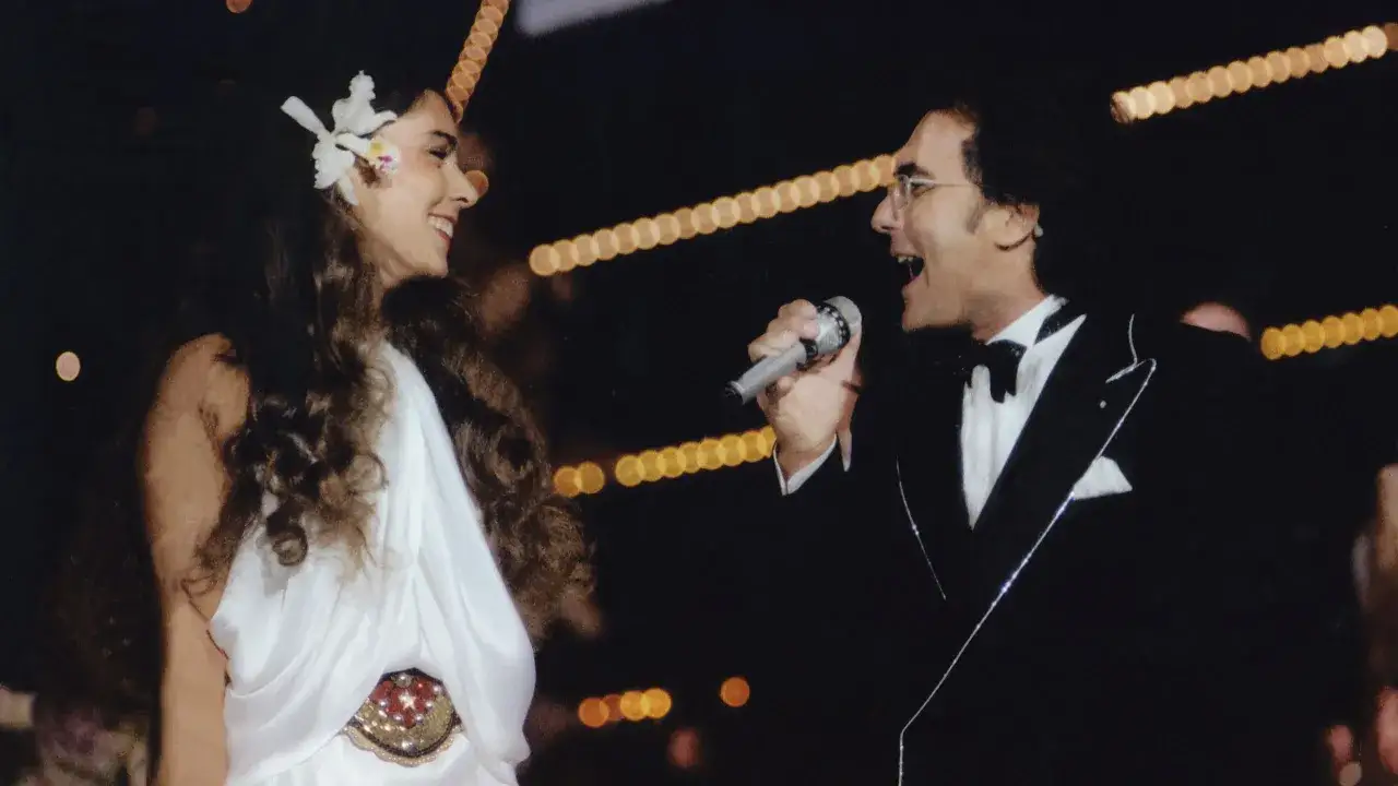 Un uomo in smoking canta al microfono, mentre una donna con un fiore tra i capelli sorride. Sembra l'inizio di una bellissima canzone d'amore.