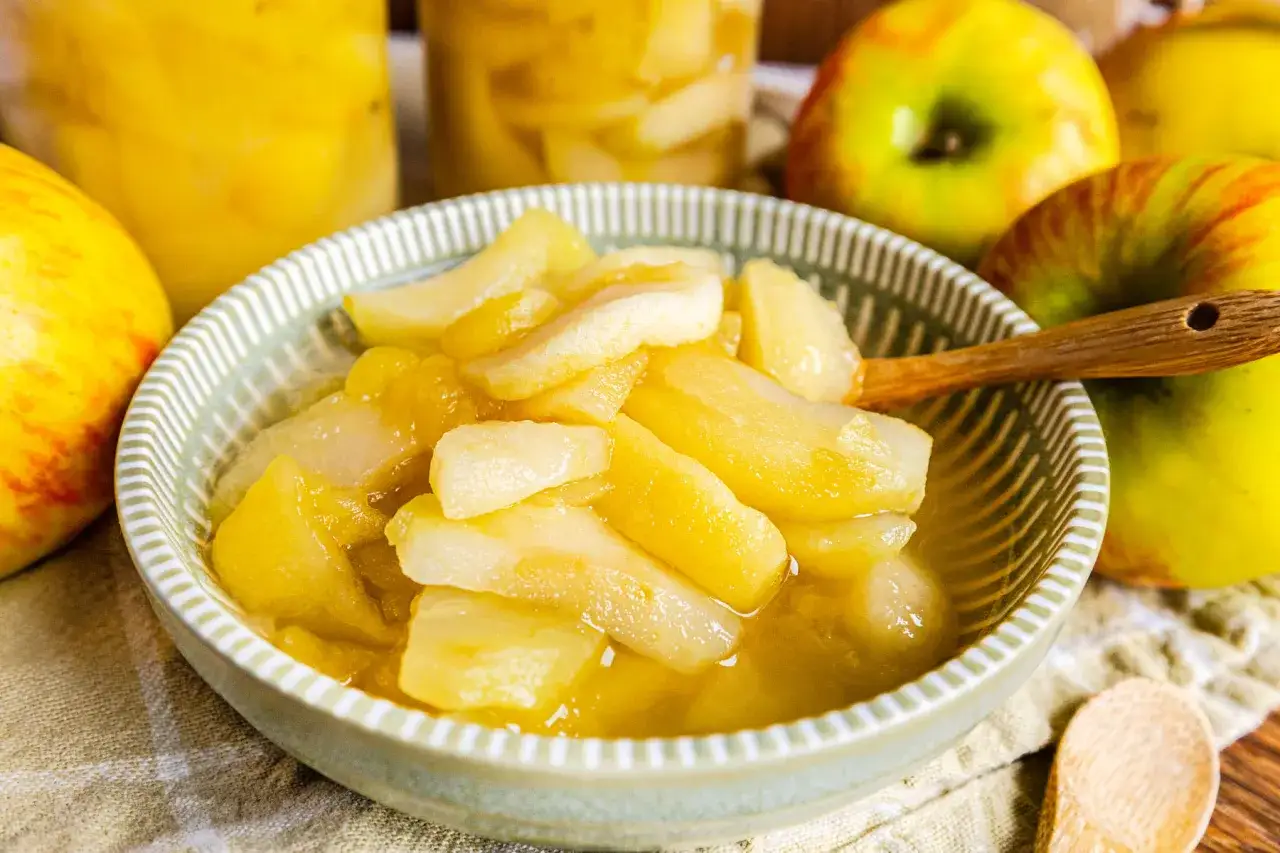 Schon fertig: Apfelkompott einkochen für den Winter. Frische Äpfel und ein Holzlöffel daneben.