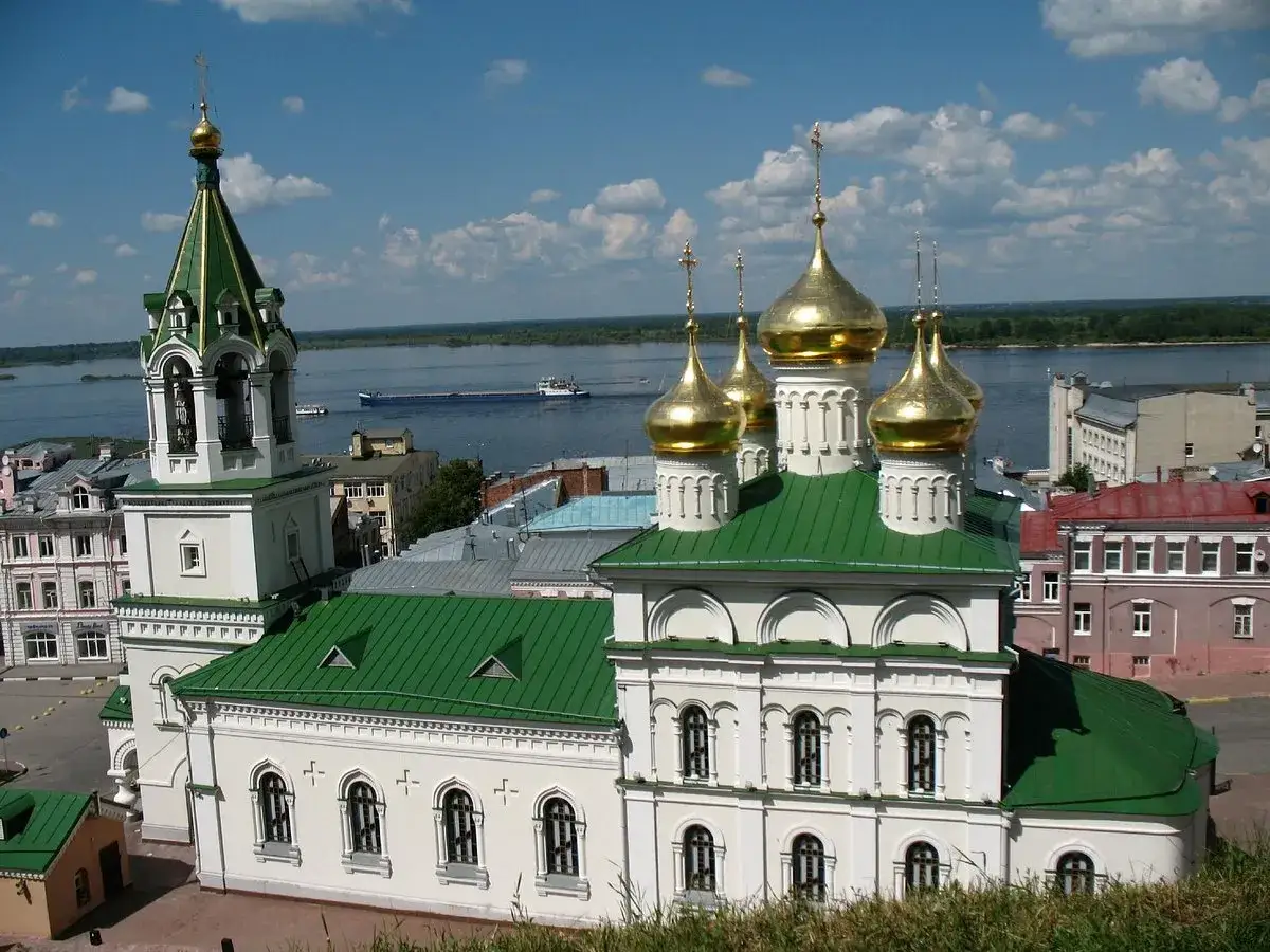 Vit kyrka med gr&ouml;nt tak och gyllene kupoler vid en flod. En klocktorn reser sig bredvid. En vy som kan finnas p&aring; en **Novgorod karta**.