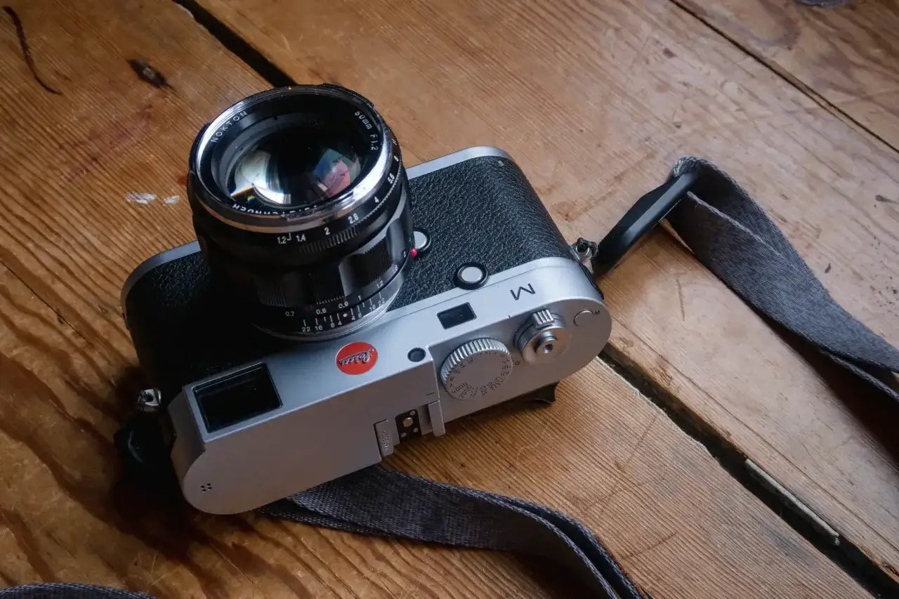 A silver Leica M 240 camera with a Nokton 50mm f/1.2 lens sits on a wooden surface.