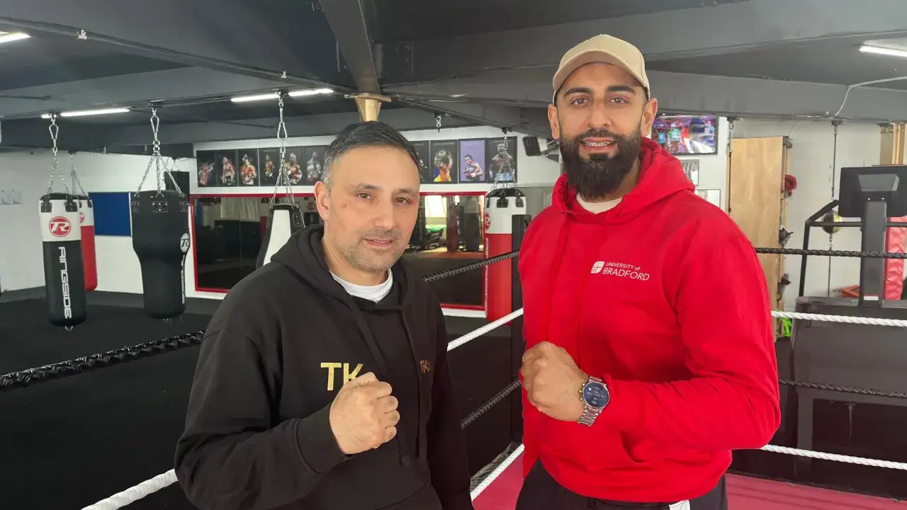 Two men in a boxing gym, one in a black hoodie, the other in a red University of Bradford hoodie. They stand ready, fists clenched, dispelling myths that boxing lowers IQ.