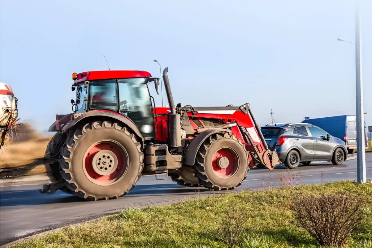 Czerwony traktor z ładowaczem na drodze, obok samochód osobowy i dostawczy. Kategoria t prawo jazdy.