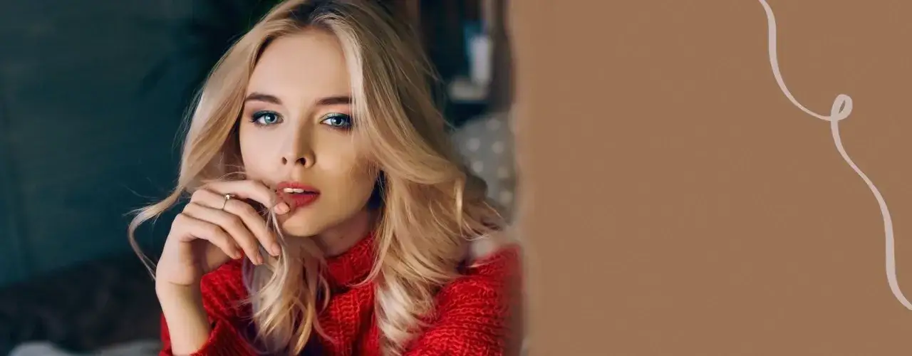 Blondynka w czerwonym swetrze z makijażem oczu i ust. Zastanawia się, czym utrwalić makijaż, by wyglądał świeżo przez cały dzień.