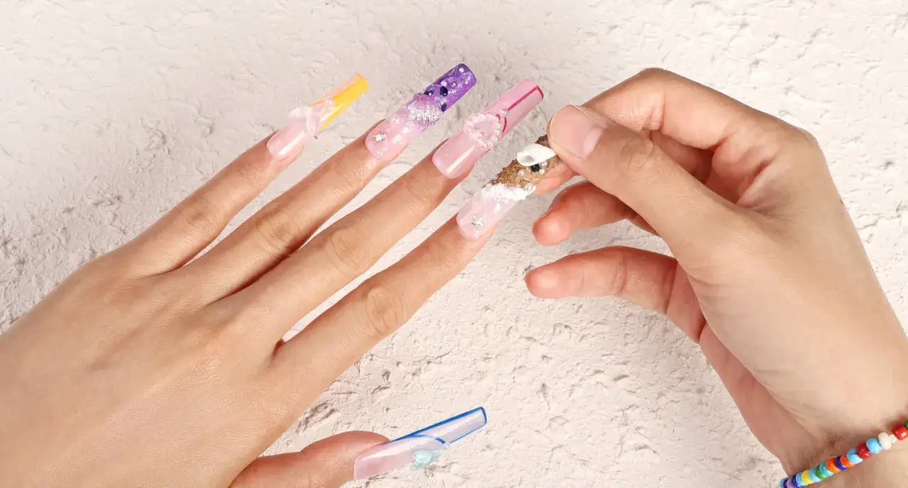 Händer med långa, dekorerade press on nails i olika färger och mönster, som pärlor och snäckor.