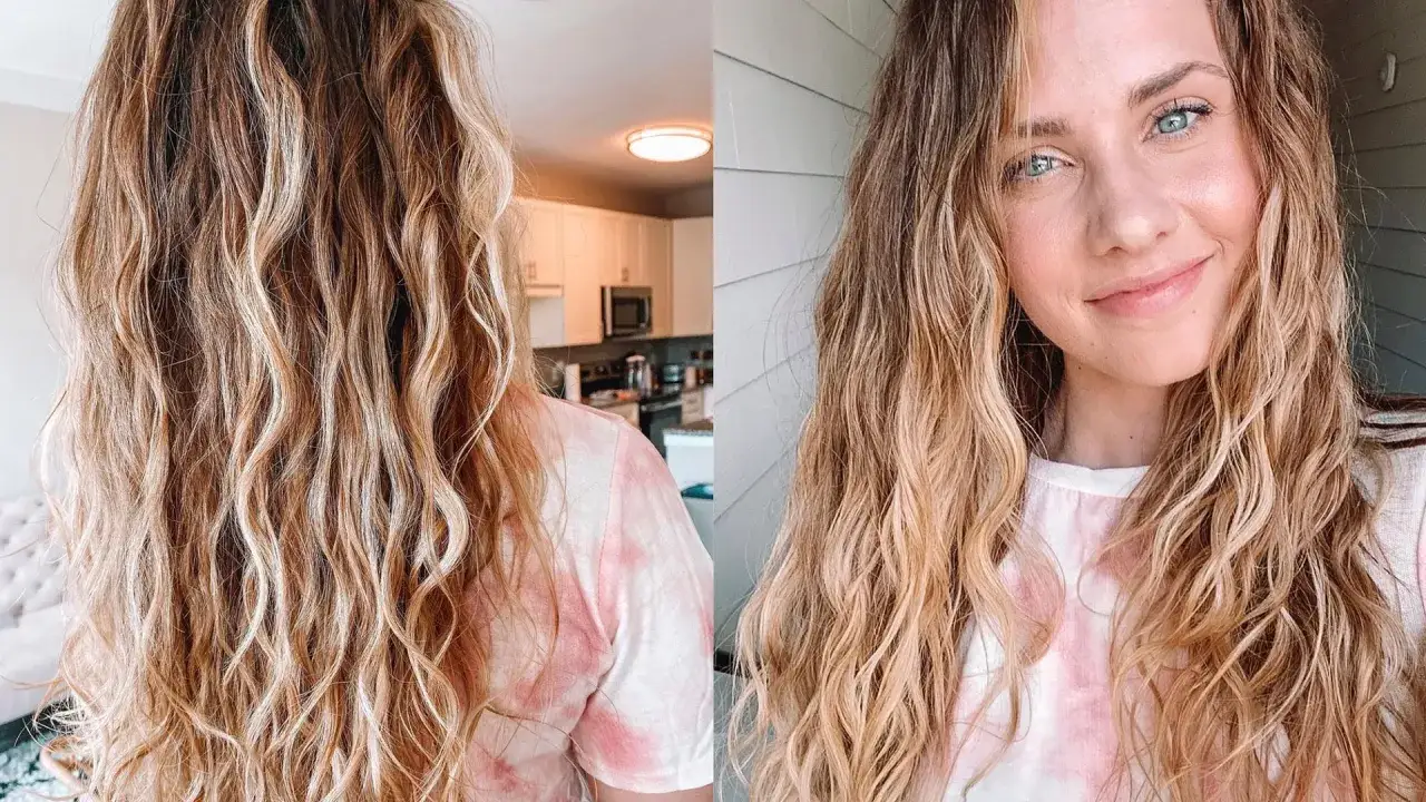 Kobieta z falowanymi, blond włosami, które mają lekki **frizz**. Uśmiecha się do aparatu, w tle kuchnia i elewacja domu.
