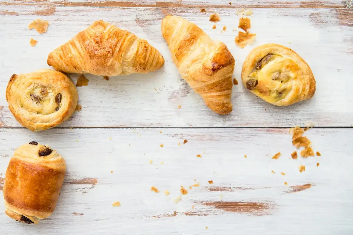 Croissants et petits pains aux raisins, des d&eacute;lices de p&acirc;te feuillet&eacute;e dor&eacute;e, &eacute;parpill&eacute;s sur une table en bois blanc.