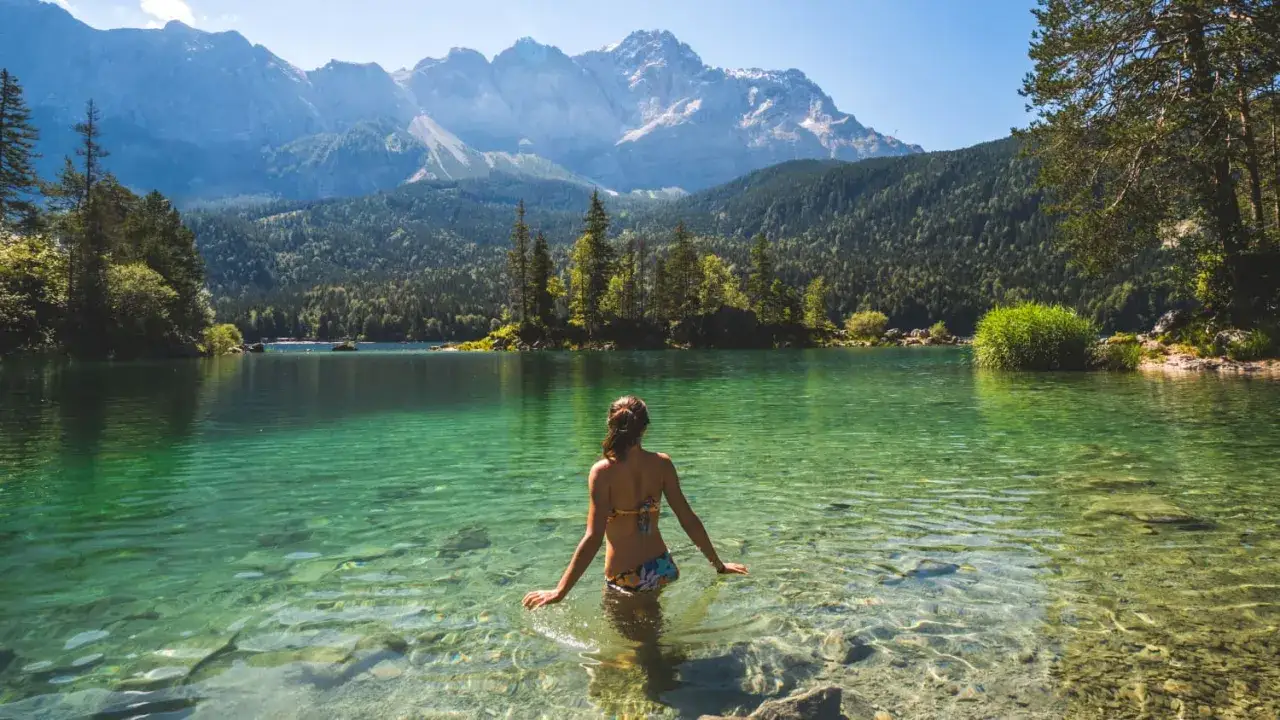 Frau im kristallklaren Wasser eines Bergsees in Deutschland, umgeben von W&auml;ldern und majest&auml;tischen Gipfeln. Ein idyllischer Ort f&uuml;r Badeseen Deutschland.