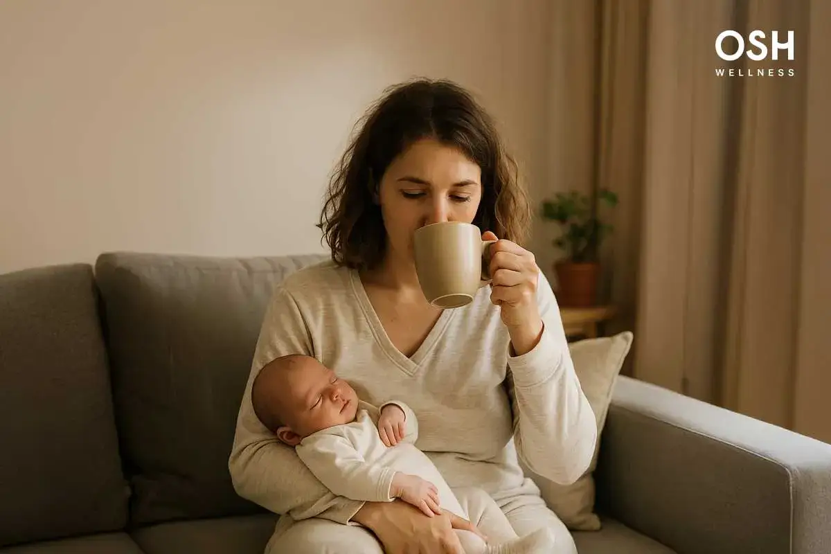 En mamma dricker kaffe medan hon ammar sin sovande bebis. Koffein amning kan vara en balansgång.
