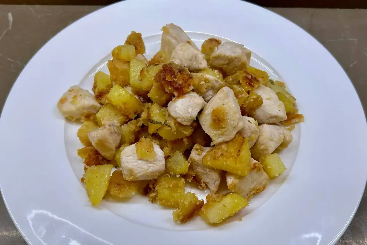 Un saporito pollo in umido con patate croccanti, servito su un piatto bianco.