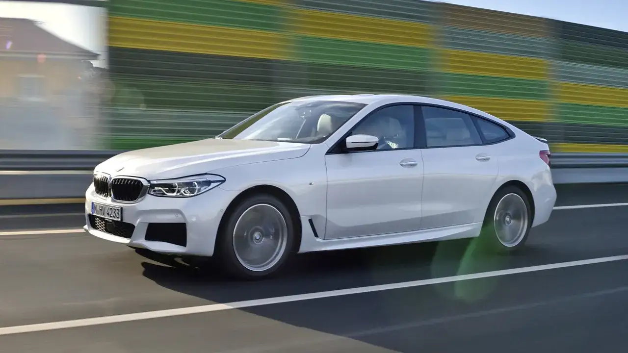 Białe BMW 640i pędzi autostradą, mijając kolorowe ekrany dźwiękochłonne.