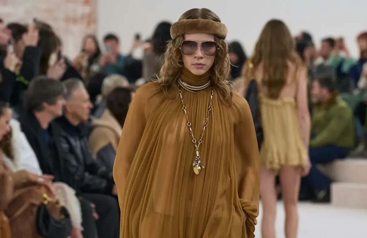 Mannequin au style bohème, portant une robe fluide ocre, un bandeau en fausse fourrure et de grandes lunettes de soleil.