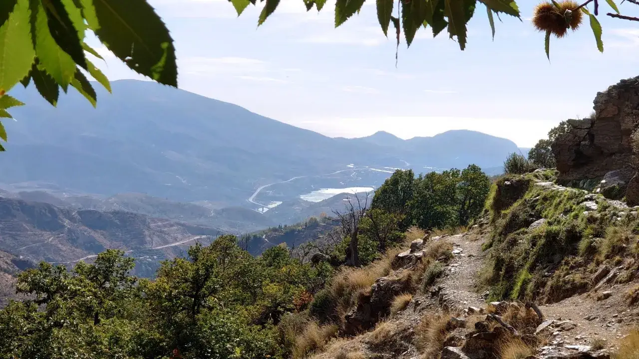 Sendero rocoso con vistas a montañas y un embalse, ideal para rutas senderismo Alpujarra.