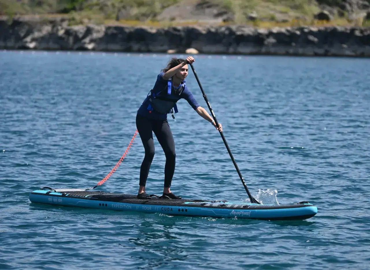 Donna con giacca salvagente pratica la tecnica sup, pagaia nell'acqua blu con una tavola gonfiabile.