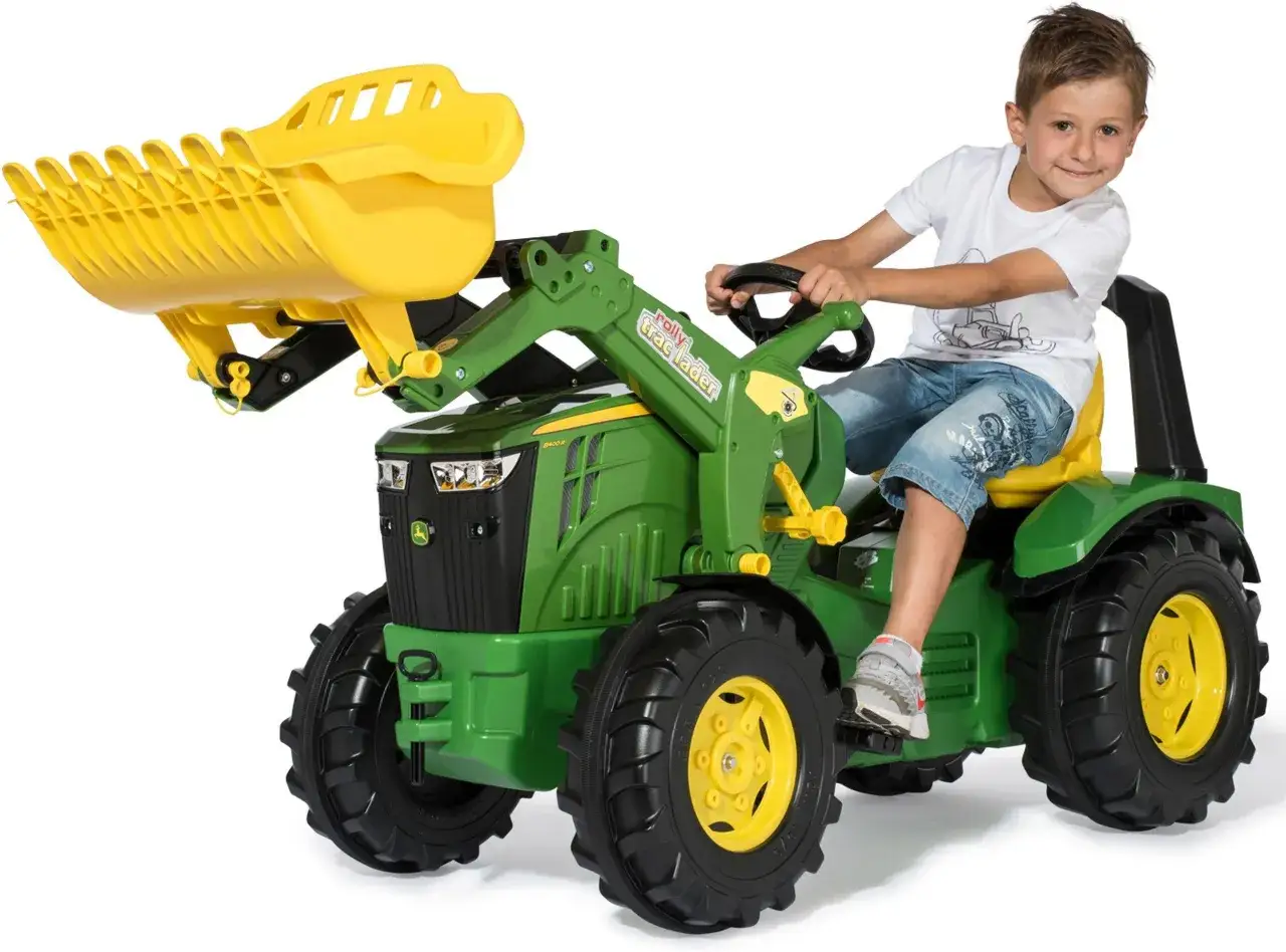 Chłopiec siedzi na zielonym mini traktorze John Deere z żółtą ładowarką.