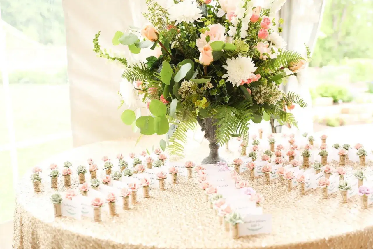 Marque place fleur, petits cactus et roses en tissu sur une table recouverte d'une nappe à paillettes dorées, devant un bouquet de fleurs.