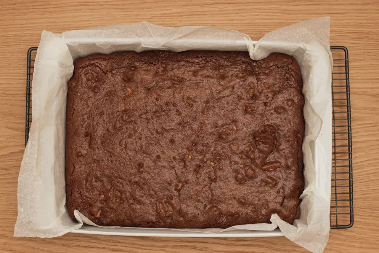 Brownie recién horneado, listo para enfriar. La superficie crujiente y los trozos de nuez prometen una deliciosa receta de brownie esponjoso.