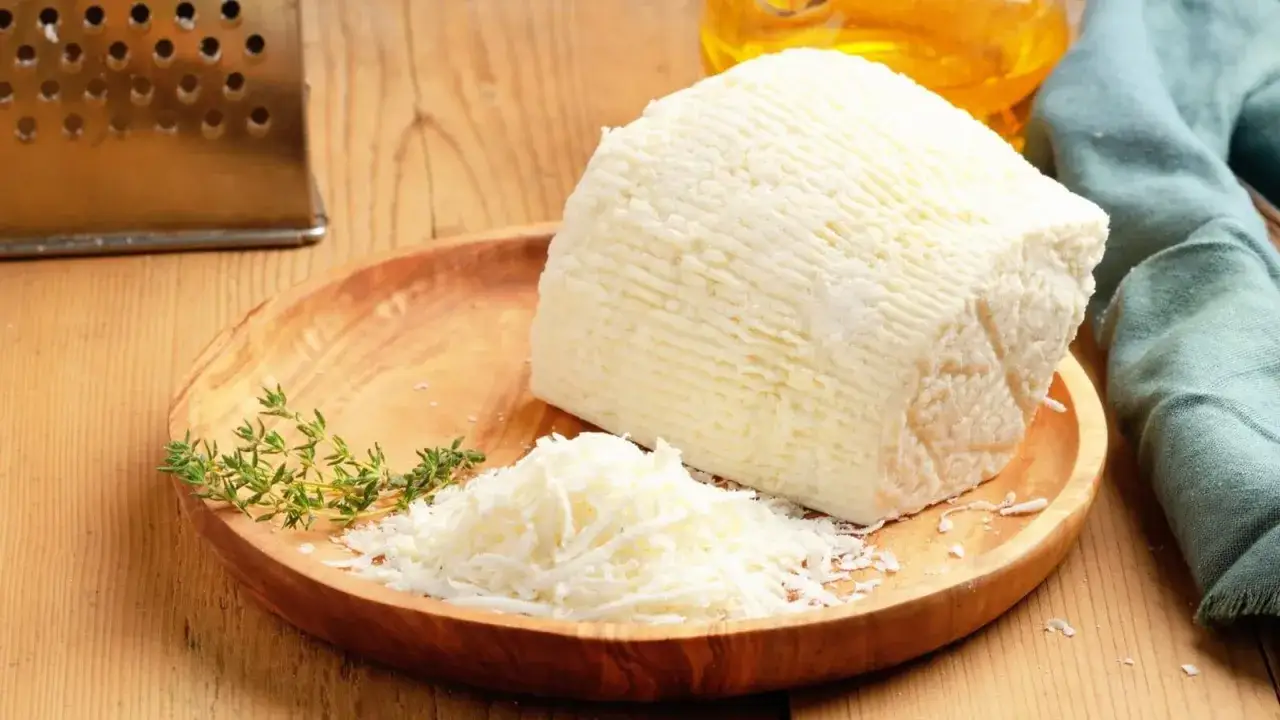 Ricotta salata grattugiata e intera su un piatto di legno, con timo. Un ingrediente saporito, utile per conoscere le ricotta salata calorie.